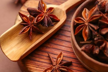 Ahşap tahta tahtada bir kase aromatik yıldız anason ve renkli arka planda kepçe, yakın plan.