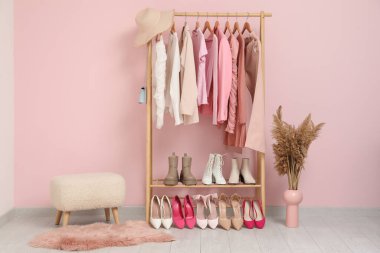 Giysiler, ayakkabılar ve pembe duvarın yanında beyaz bir puf.