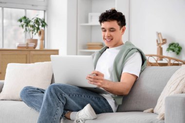 Evdeki kanepede dizüstü bilgisayarla çalışan genç adam.