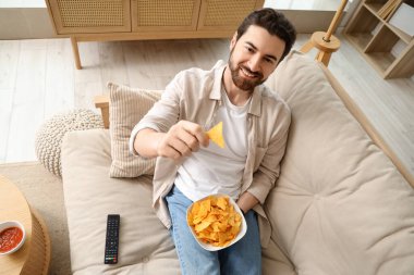 Adam evde TV izlerken lezzetli nacho yiyor.