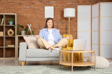 Evdeki kanepede meditasyon yapan gülümseyen genç kadın.