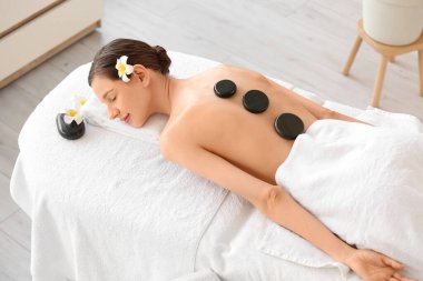 Güzel genç bir kadın masaj masasında sıcak taşlarla rahatlıyor.