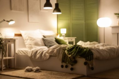 Yatak odasının bulanık görüntüsü, katlanır ekran, masalar ve geceleri parlayan lambalar.