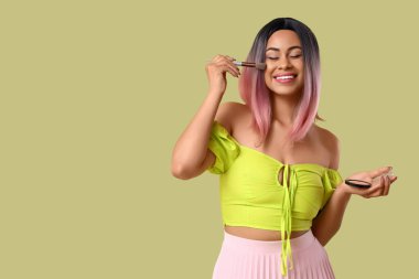 Makyaj fırçası ve yeşil arka planı olan şık peruklu güzel bir Afro-Amerikalı kadın.