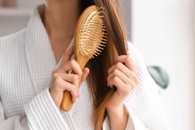 Güzel genç bir kadın banyoda saçını tarıyor.