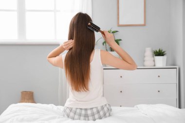 Güzel genç bir kadın yatak odasında saçını tarıyor.
