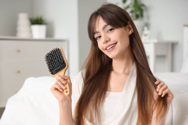 Güzel, genç, mutlu, saç fırçalı bir kadın. Yatak odasının yanında oturuyor.