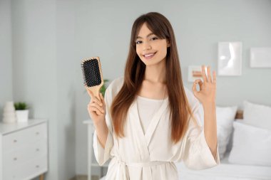 Güzel, genç, mutlu, saç fırçalı bir kadın. Yatak odasında güzel bir jest yapıyor.