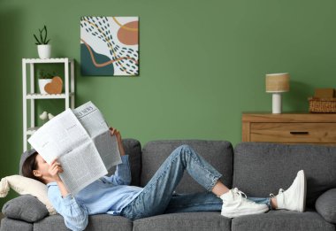 Young woman reading newspaper on sofa at home