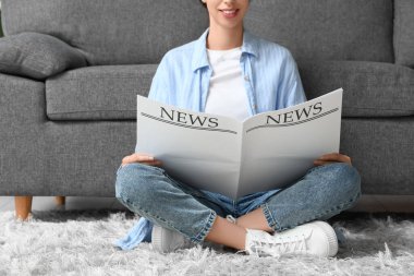 Evdeki halıda boş gazete okuyan genç kadın.