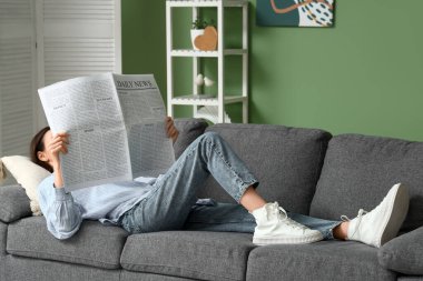 Young woman reading newspaper on sofa at home