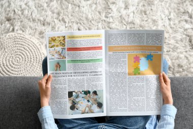 Evdeki kanepede gazete okuyan genç bir kadın.