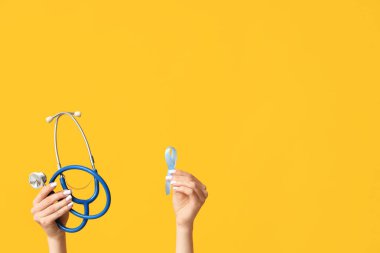 Sarı arka planda mavi kurdeleli ve steteskoplu kadın eller. Prostat Kanseri Farkındalığı Ayı