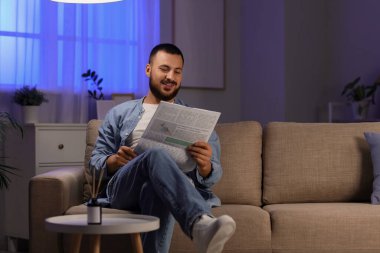 Evdeki kanepede gazete okuyan yakışıklı bir adam.