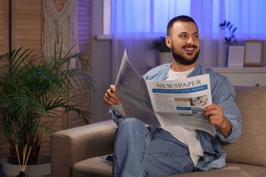 Evdeki kanepede gazete okuyan yakışıklı bir adam.