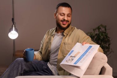 Çay fincanı ve gazeteli genç adam akşamları evdeki kanepede oturuyor.