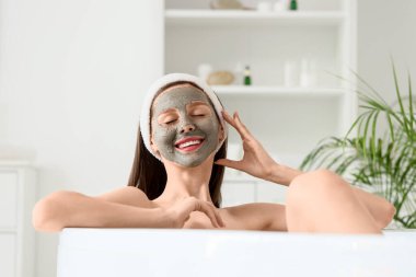 Evdeki küvette yatan kilden maskeli güzel, genç ve mutlu bir kadın.