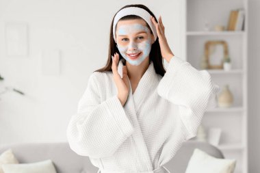 Evde kilden maskeli, bornozlu, güzel, genç bir kadın var.