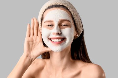 Gri arka planda kilden maskesi olan güzel, mutlu genç bir kadın.