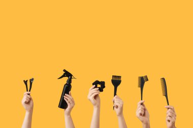 Turuncu arka planda farklı kuaför malzemelerine sahip kadın elleri.