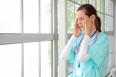 Kliniğin penceresinin yanında stresli bir kadın stajyer.
