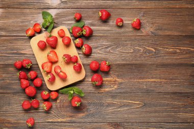 Tahta kesme tahtası olgun çilekler ve ahşap arka planda nane yaprakları