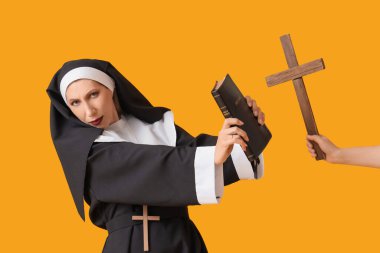 İncil 'i olan bir rahibe gibi giyinmiş olgun bir kadın ve sarı arka planda tahta haç tutan bir kadın. Cadılar Bayramı