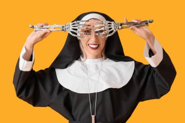 Sarı arka planda iskelet elleri olan, rahibe gibi giyinmiş mutlu olgun bir kadın. Cadılar Bayramı