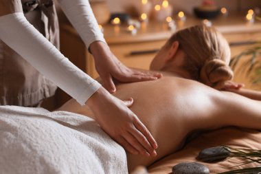 Koyu kaplıca salonundaki kanepede sırt masajı yaptıran güzel genç bir kadın.