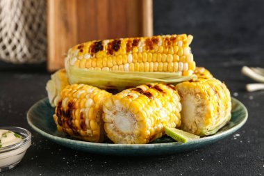 Lezzetli ızgara mısır koçanı ve siyah arka planda bir kase sos.