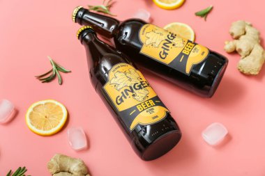 Taze zencefilli bira, biberiye, limon dilimleri ve pembe arka planda buz küpleriyle kompozisyon, yakın plan.