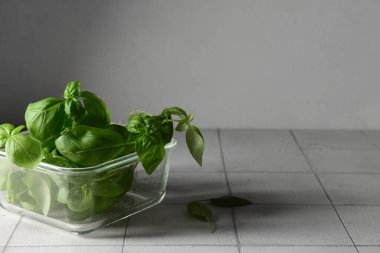 Beyaz fayans masasında taze yeşil fesleğenli cam kase.