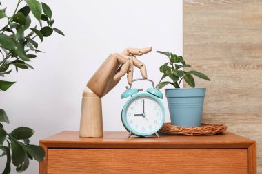 Çalar saati, ahşap eli ve saksısı olan bir komodin.