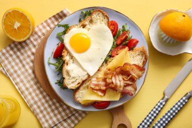 Lezzetli kızarmış yumurta, kruvasan, pastırma, domates ve sarı arka planda bir bardak meyve suyu.