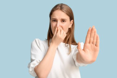 Mavi arka planda kötü kokan genç bir kadın.