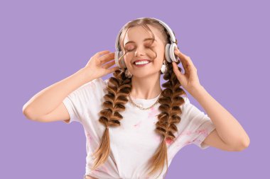 Kulaklıklı mutlu, genç bir kadın leylak arka planda müzik dinliyor.