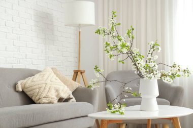 Sehpanın yanındaki sehpanın üzerinde çiçek açan bir vazo ve şık bir oturma odasında koltuk.