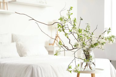 Sehpanın üzerinde çiçek açan bir vazo beyaz şık bir yatak odasında, rahat bir yatağın yanında, yakın plan.