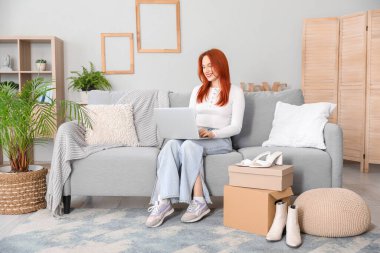 Evde yeni ayakkabıları olan dizüstü bilgisayar kullanan genç bir kadın.