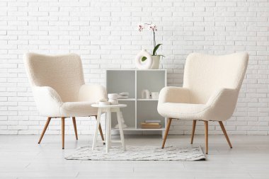 Rahat koltuklar, raf ünitesi ve beyaz tuğla duvarın yanındaki dekorasyon.