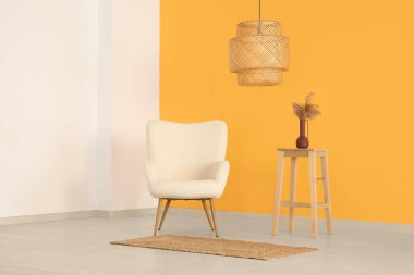 Sarı duvarın yanında konforlu koltuk, lamba ve vazo.