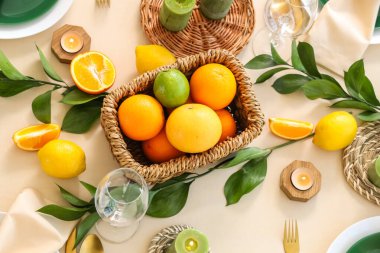 Narenciye meyveleri, yanan mumlar ve açık masa örtüsünün üzerindeki yeşil yapraklarla dolu güzel bir masa.