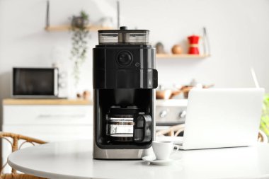 Mutfaktaki masada fincanı ve laptopu olan modern kahve makinesi.