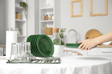 Kadın elleri mutfaktaki yemek masasına temiz tabaklar koyuyor.