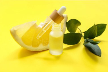 Bir şişe kozmetik yağı, yeşil yapraklar ve sarı arka planda bir parça taze zeytin, yakın plan.