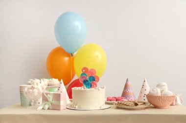 Beyaz duvara karşı pasta, şeker ve doğum günü partisi için dekorasyon masası.