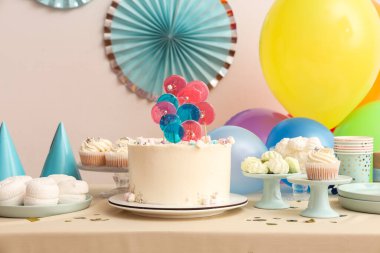 Beyaz duvara karşı pasta, şeker ve doğum günü partisi için dekorasyon masası.
