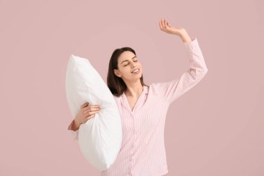 Pembe arka planda yastıklı pijamalı genç bir kadın.