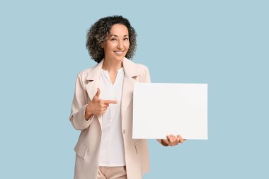 Olgun iş kadını mavi arka plandaki boş karta işaret ediyor