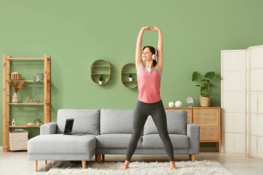 Kulaklıklı güzel bir kadın oturma odasında yoga yapıyor.